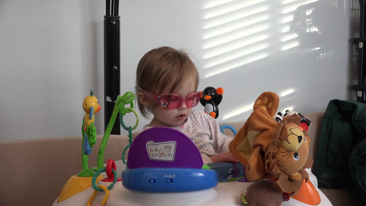 Toddler in pink sunglasses at a colorful play table.