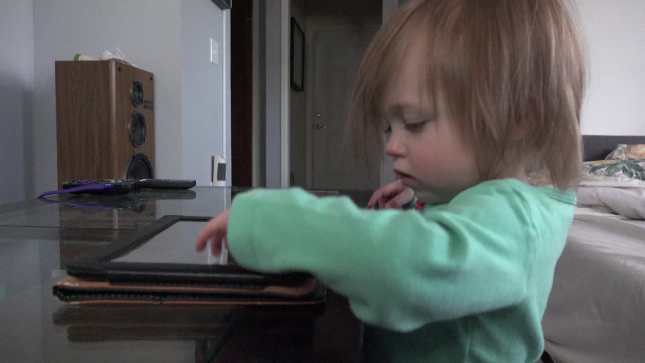 The child leans closer to the tablet in the Westminster home interior, with hair partly covering the face and one hand hovering over the screen.