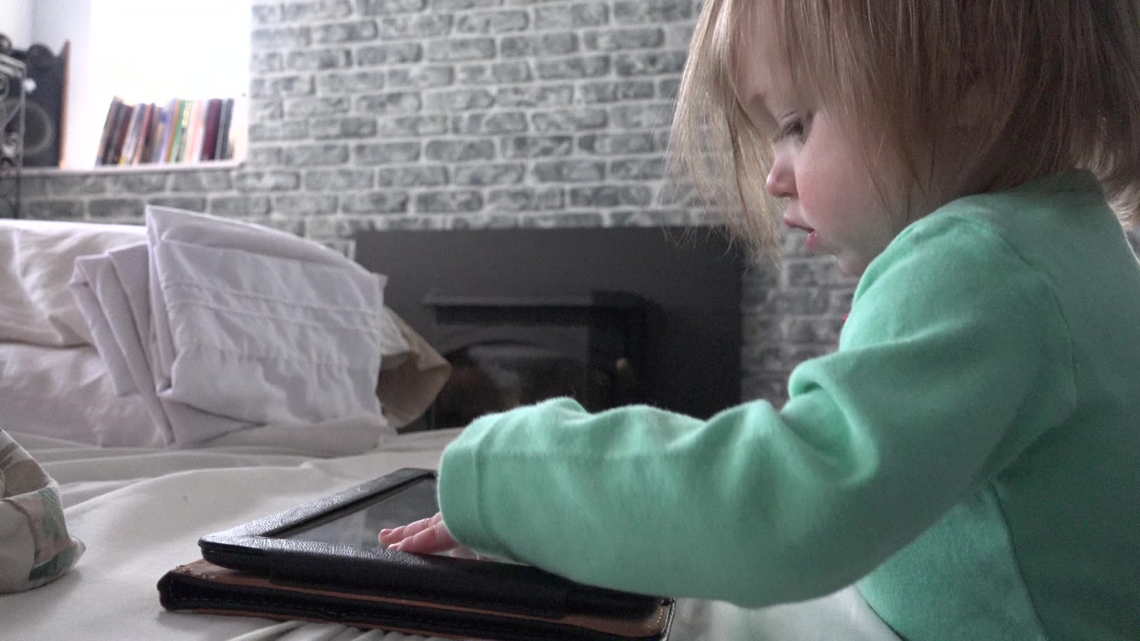 Toddler in a green top tapping an iPad on a bed.