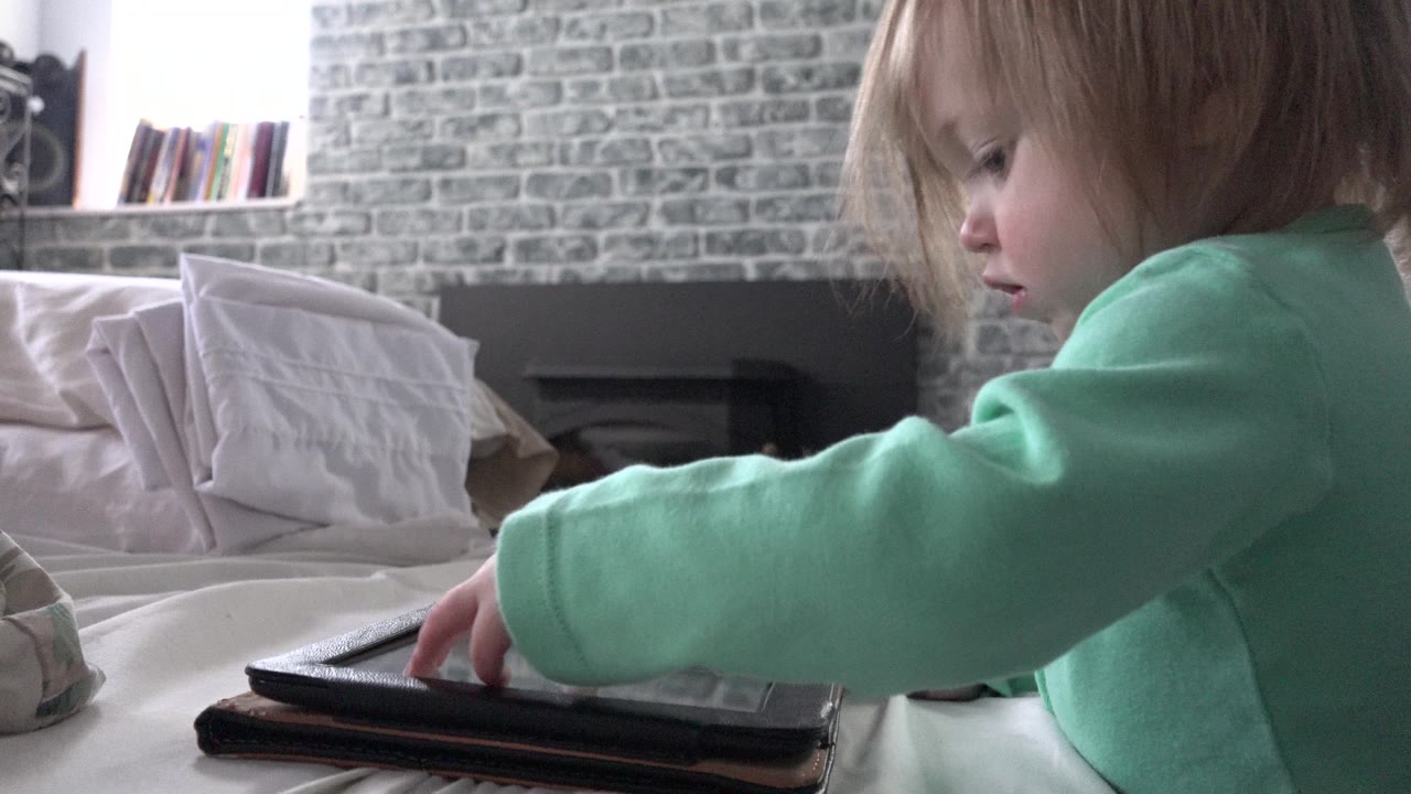 The child in Westminster, Colorado reaches farther across the iPad screen, with the tablet case in the foreground and the brick wall still visible behind.