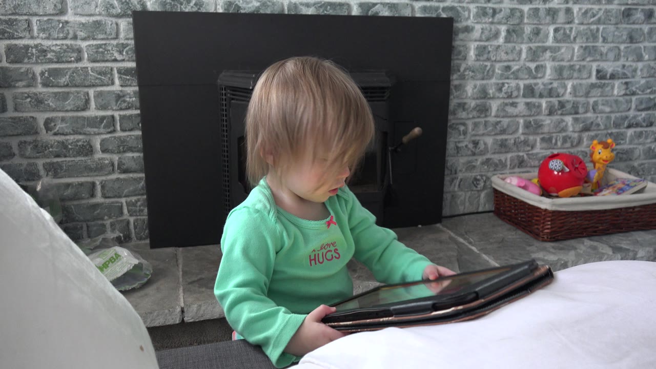 Young child holding a tablet beside a white couch and fireplace.