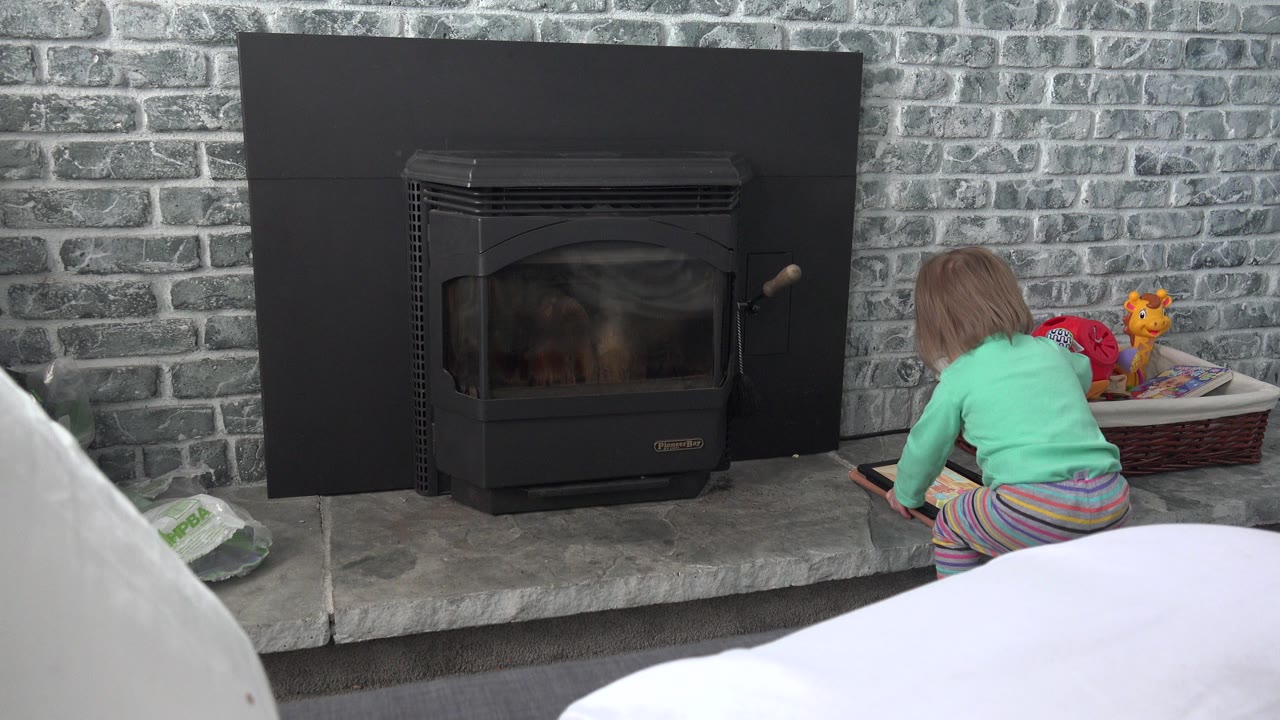 At 0:00 in Westminster, Colorado, a young child kneels on the hearth beside a tablet, with a black fireplace centered and a toy basket on the right.