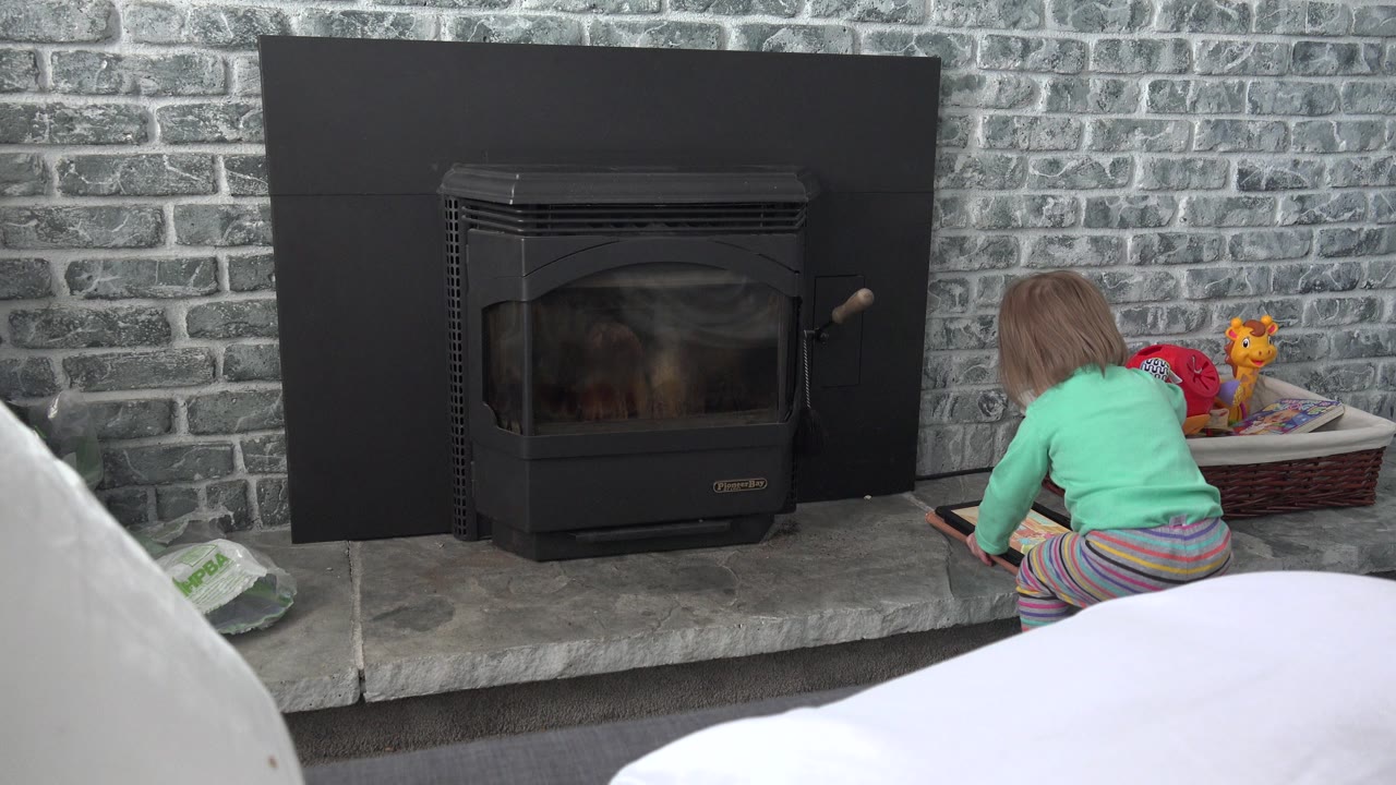 At 0:01 in Westminster, Colorado, the child stays crouched near the tablet while the colorful toy basket remains visible beside the gray brick fireplace wall.