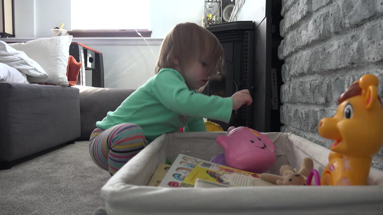 Toddler kneeling beside a toy box in a living room.
