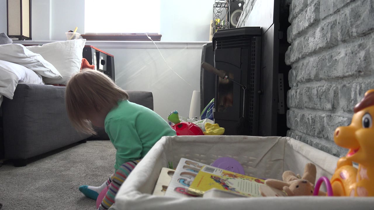Toddler sits on carpet beside a toy bin in a living room.