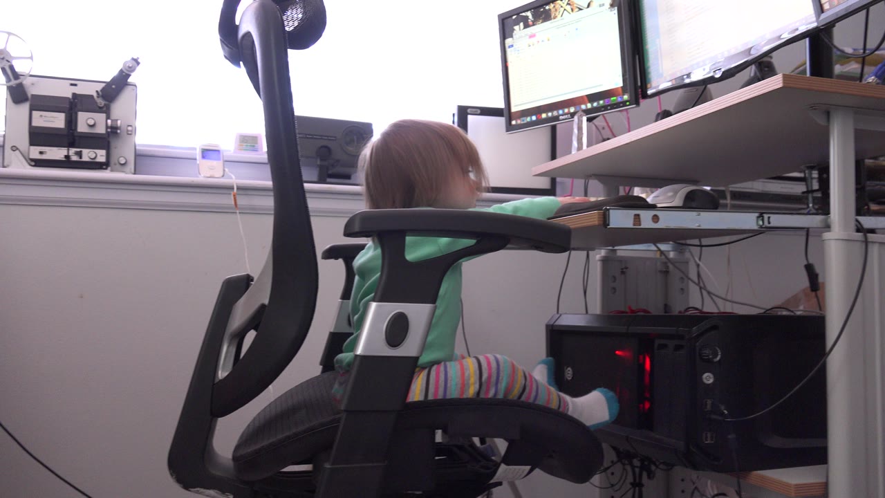 Young blond girl seated at a home office computer desk.