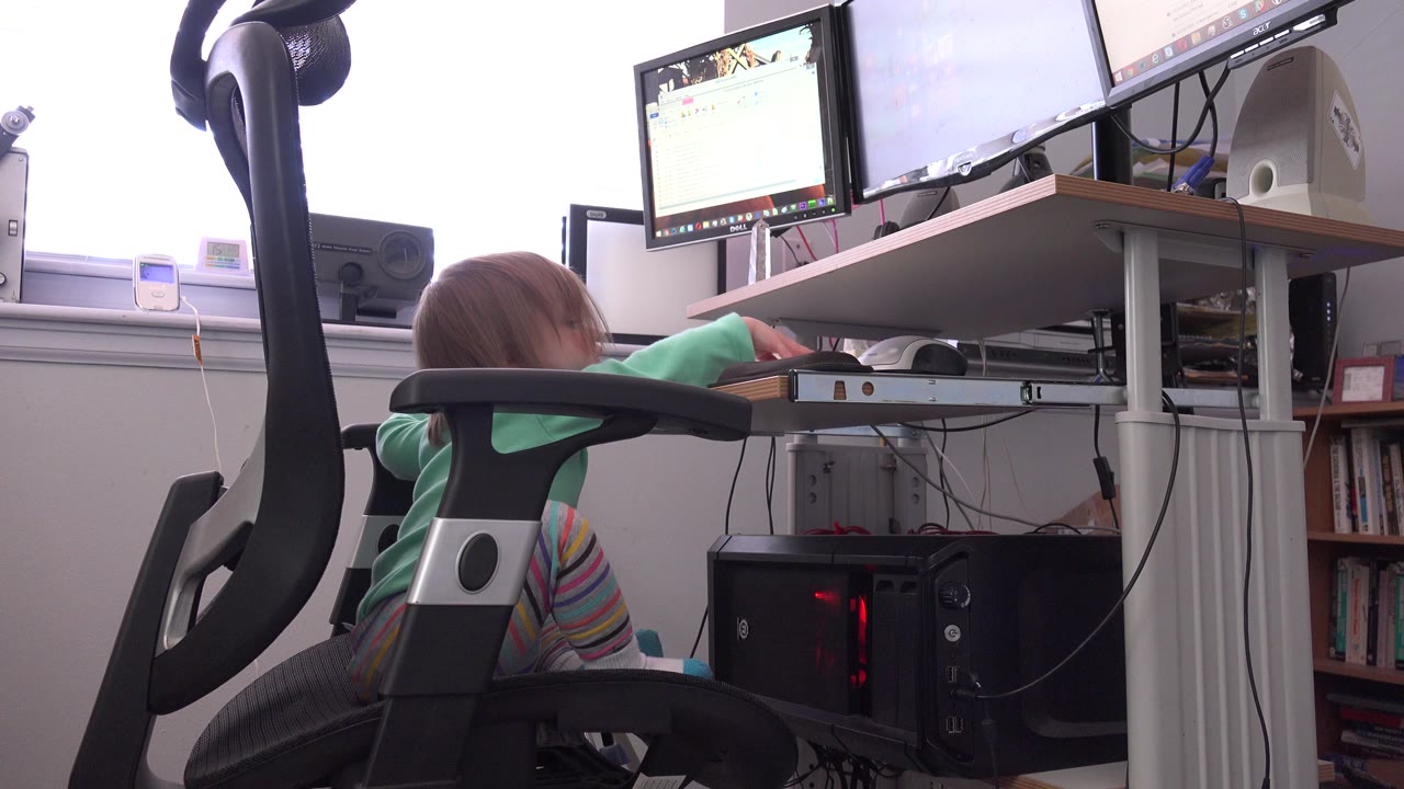 Child leaning forward in an office chair at a computer desk.
