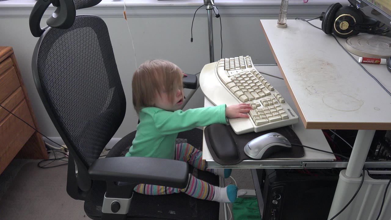 Small child in an office chair reaching toward a beige keyboard.