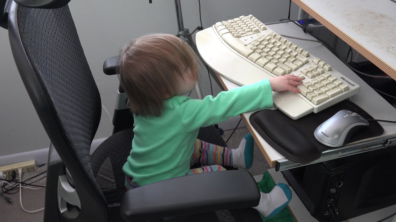 Young child seated at a desk reaching toward a beige keyboard.
