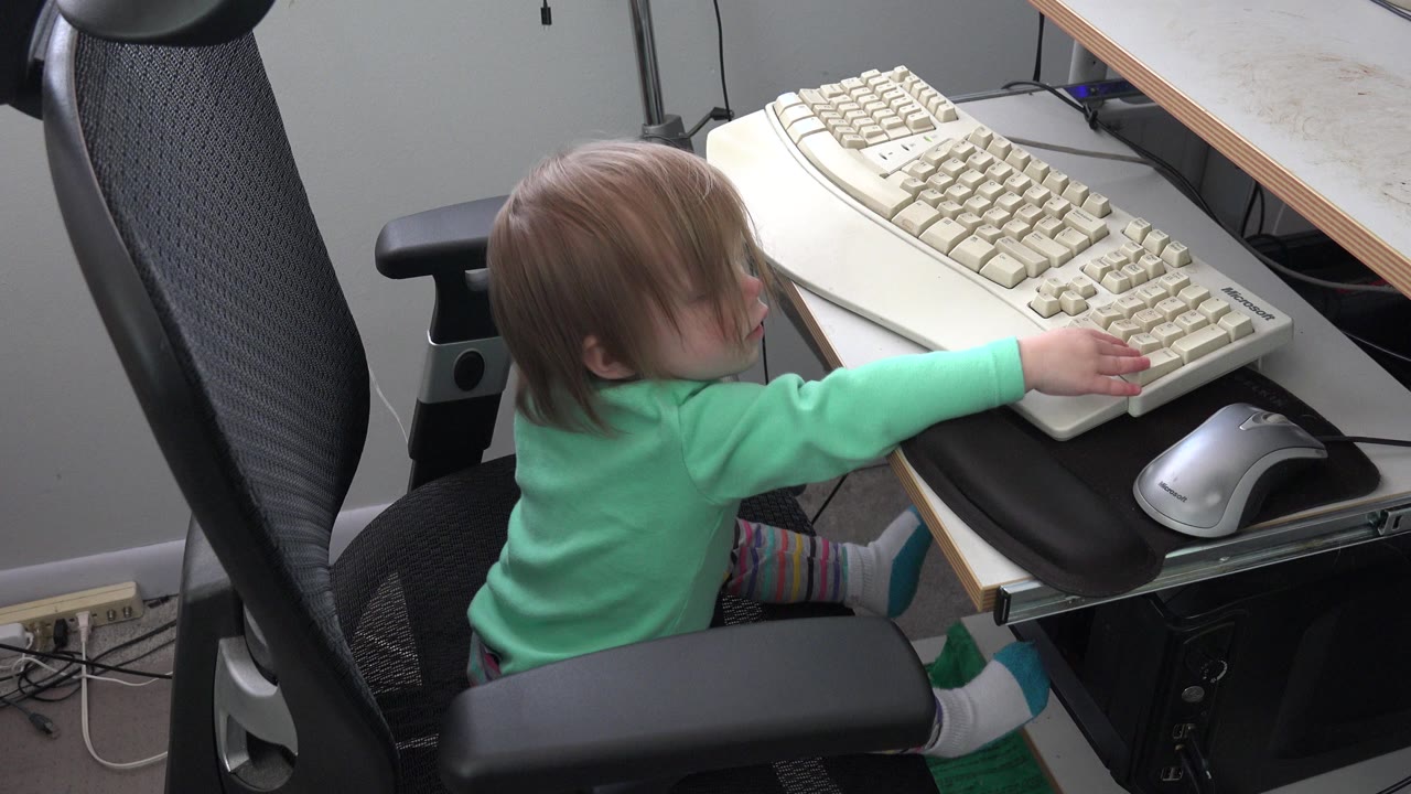 The child remains seated in the office chair in Westminster, Colorado, leaning forward with a hand near the keyboard and silver mouse.