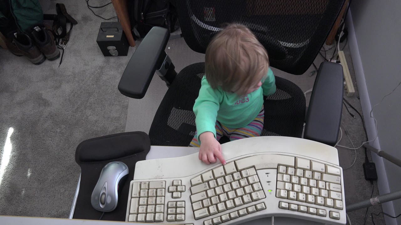 At 0:01 in Westminster, Colorado, the child keeps her gaze lowered as her fingers rest near the keyboard keys, with the office chair back filling the upper background.