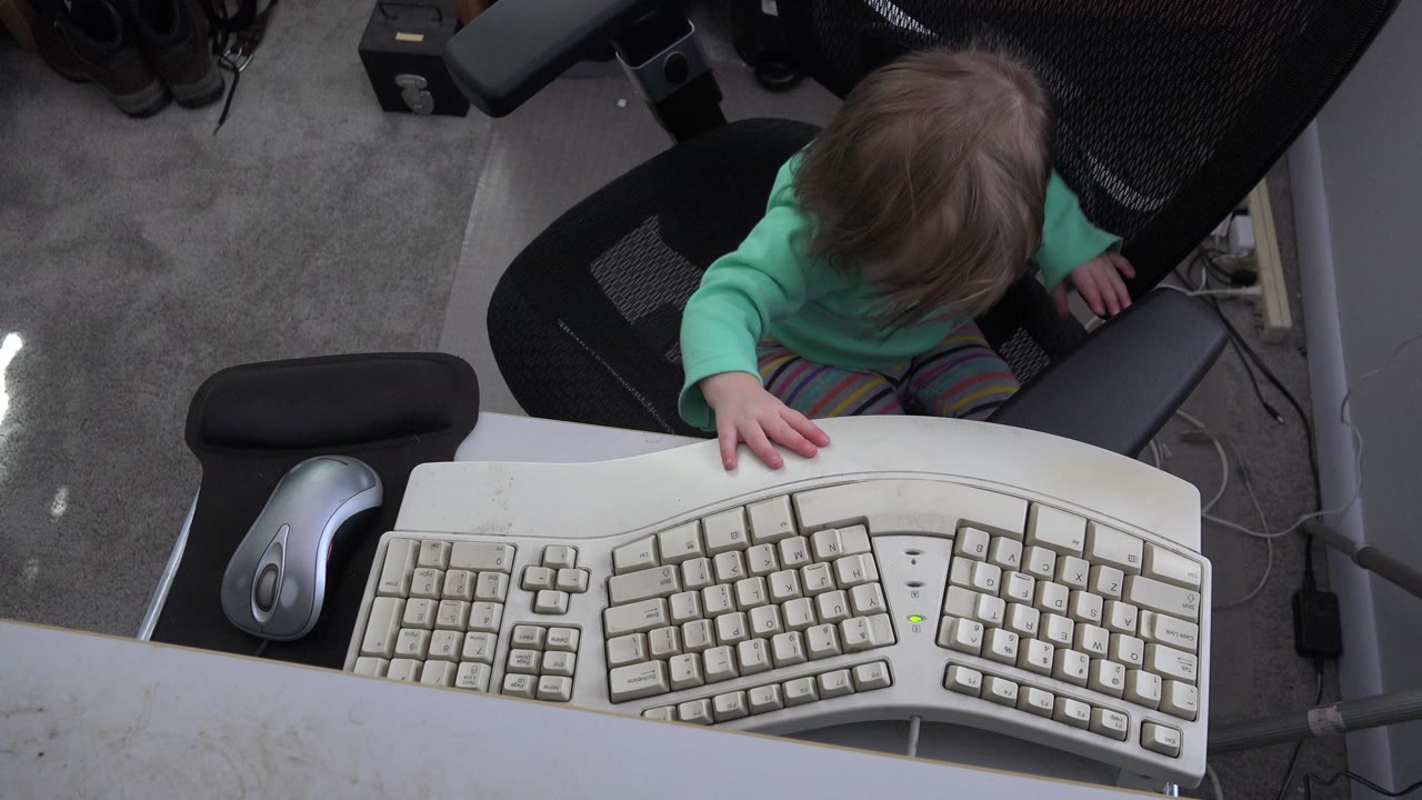 Young child seated behind a large computer keyboard at a desk.