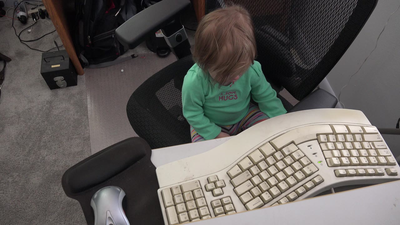 Toddler sitting behind a desk with a beige keyboard in front.