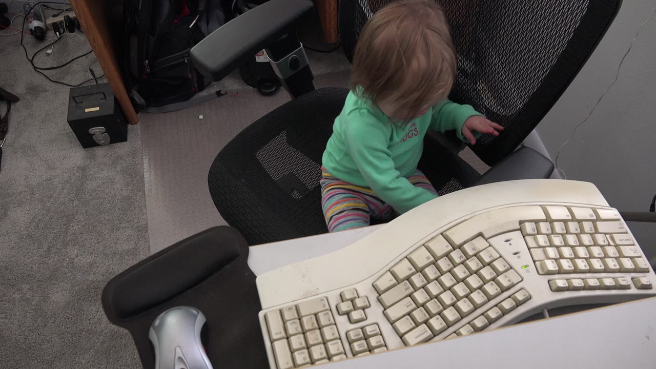At 0:01 in Westminster, Colorado, the child looks down while seated in the black office chair, with the beige keyboard spanning the lower foreground.