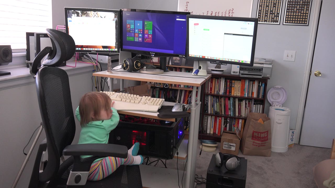 At 0:00, a young child in green pajamas sits sideways in a black office chair at a multi-monitor computer desk in a Westminster, Colorado home interior.