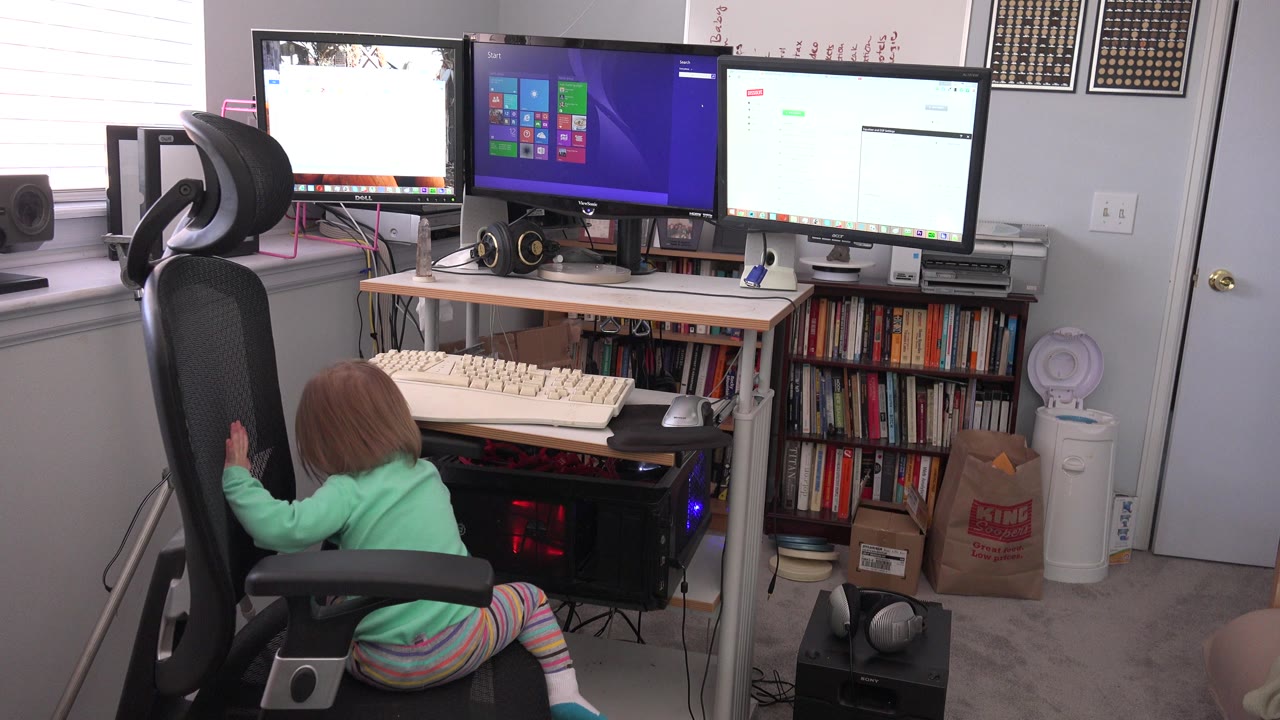 Young child reaching up beside a black office chair in a home office.