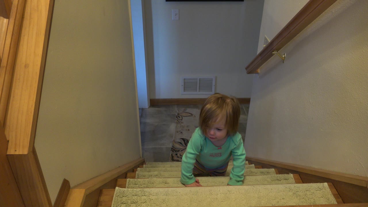 Baby in green top crawling up carpeted stairs.