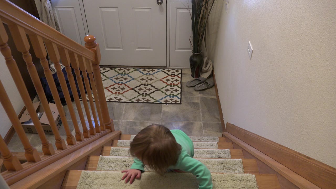 Child partly visible near the top of carpeted stairs beside a wooden railing.