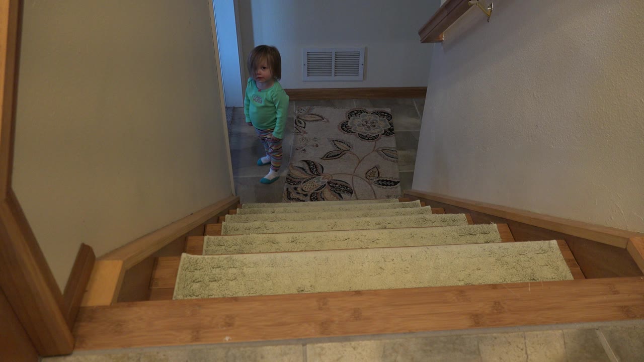 A young girl in a green top stands near a patterned rug at the bottom of a carpeted staircase in a Westminster, Colorado home.