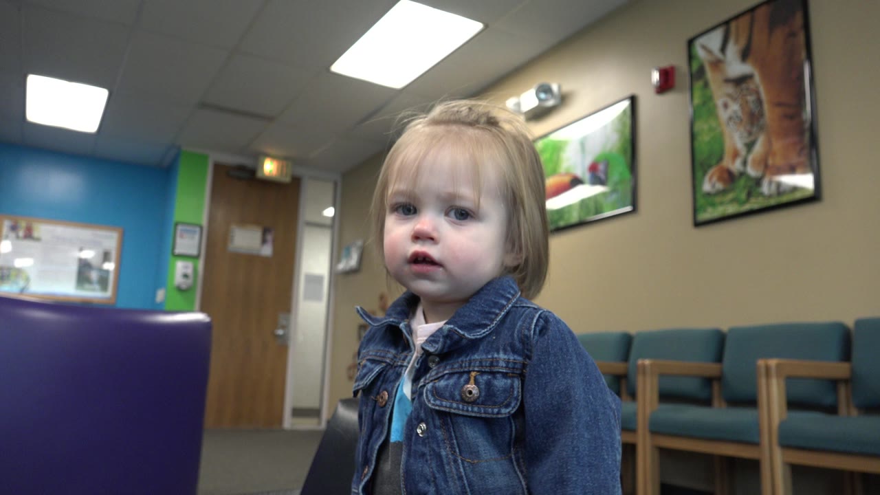 Child in denim jacket looking forward in a doctor's office waiting area.