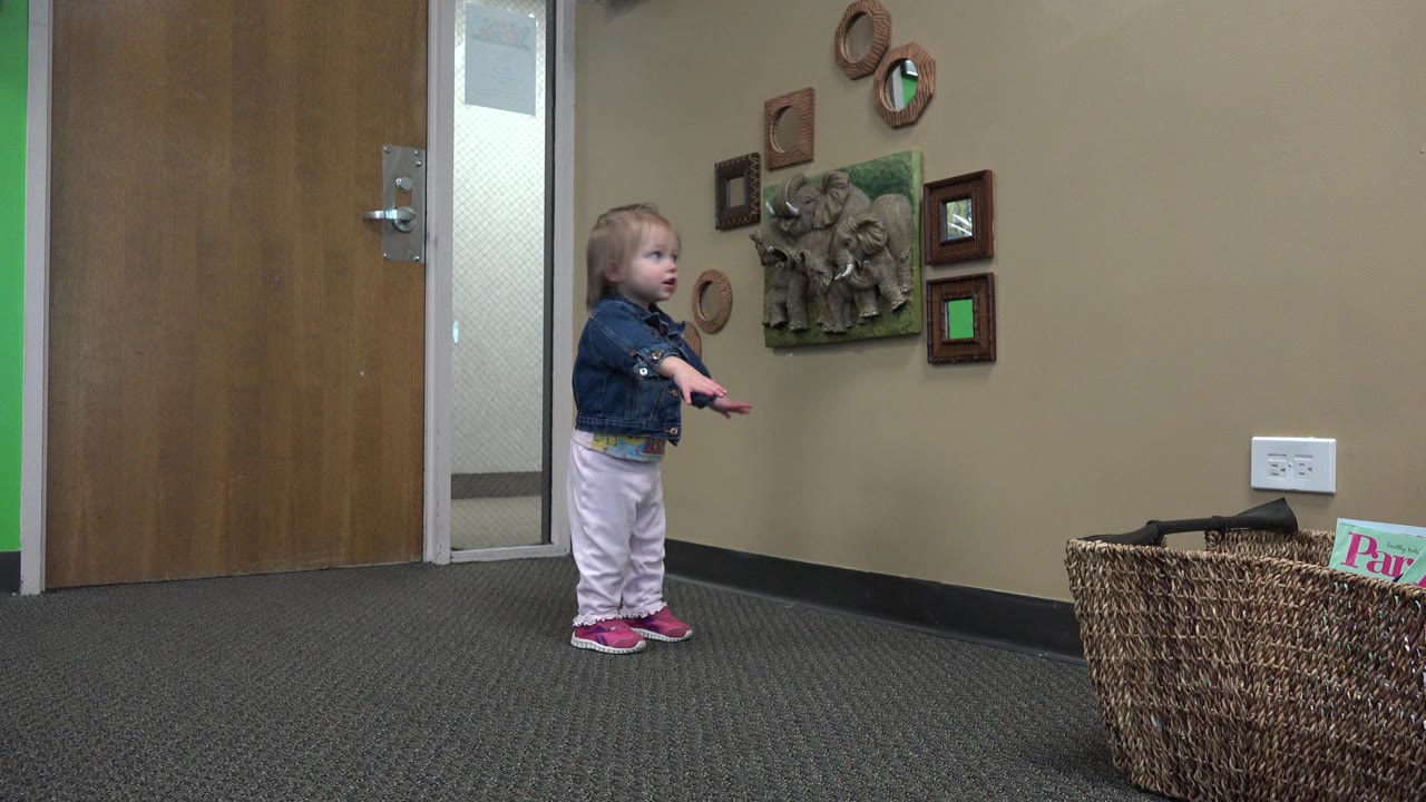 Toddler standing in a decorated lobby near a wood door.