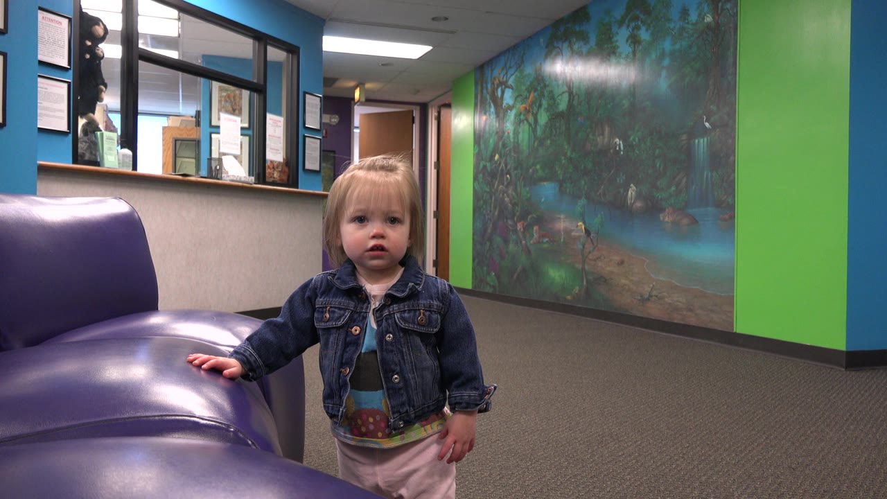 Toddler touches the purple sofa while standing in a colorful interior.