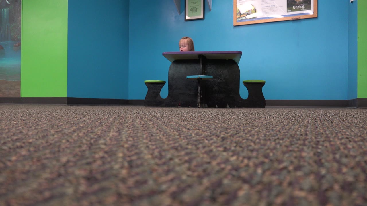 Toddler partly visible behind a small black table in a blue-walled room.