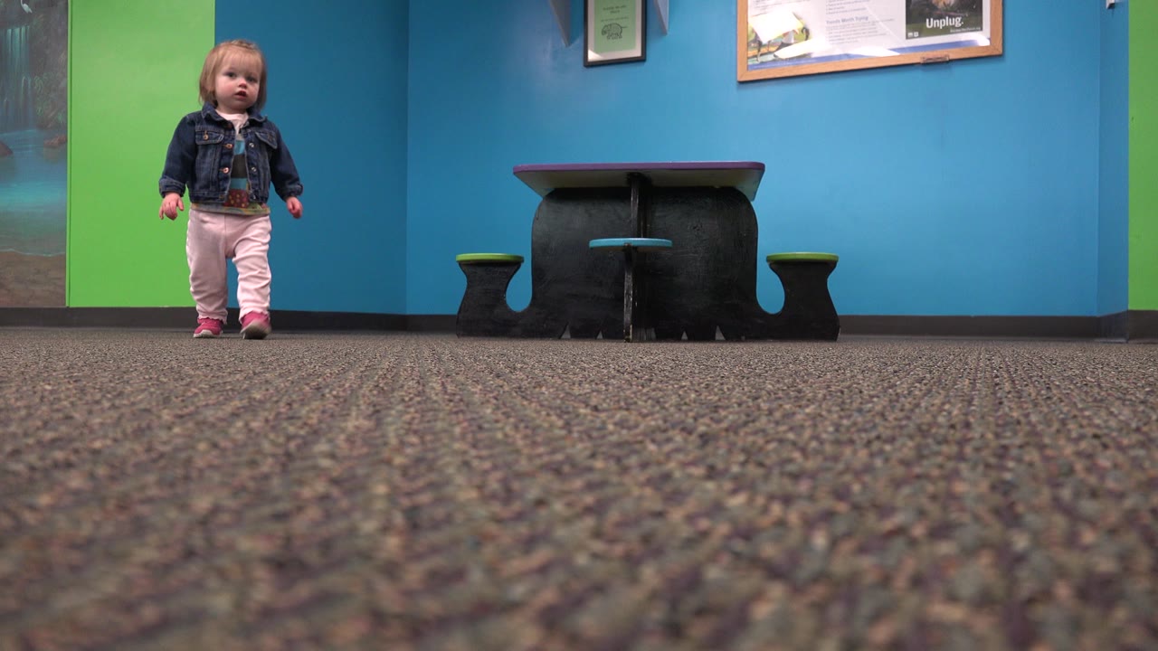 Toddler girl facing the camera in an indoor carpeted space.