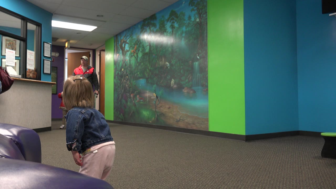 Toddler from behind near a mural wall and doorway.