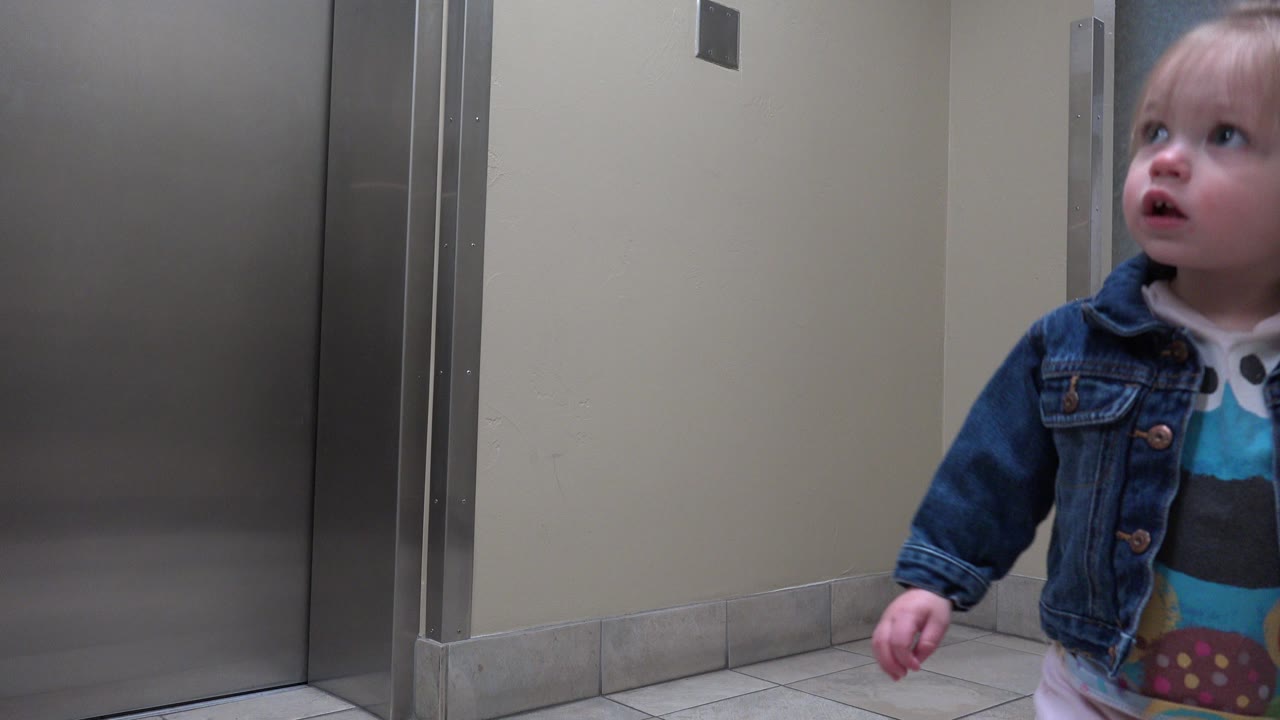 Little girl near stainless elevator doors in a corridor.