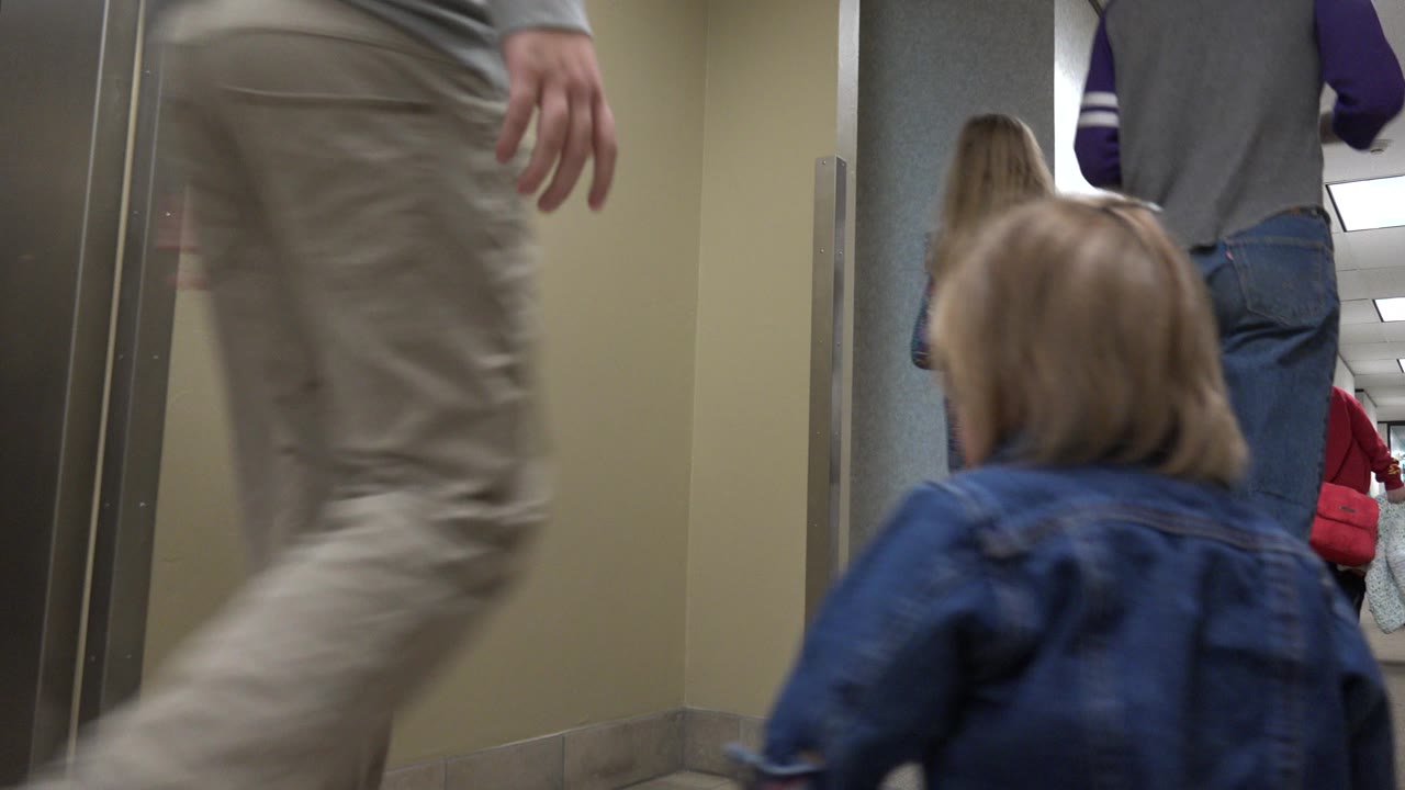 Low hallway view with an adult walking past and a toddler ahead.