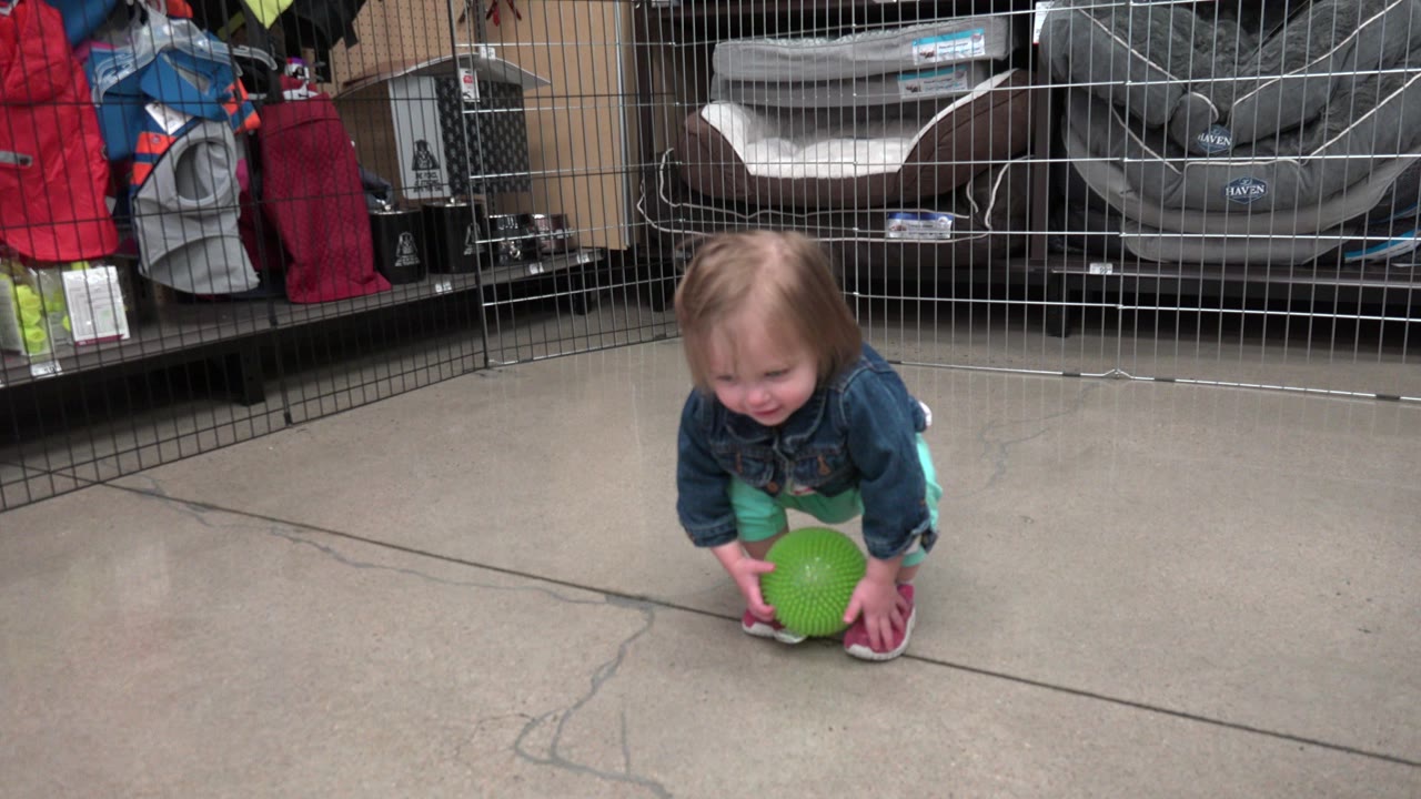Toddler girl crouching with a green ball on a concrete floor.