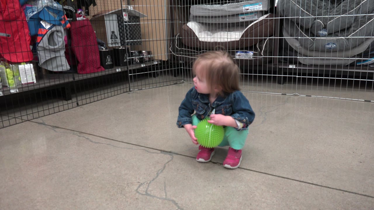 Toddler crouching with a green ball on a retail store floor.