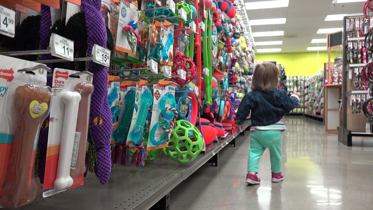 Small child standing in a toy aisle with colorful merchandise on both sides.