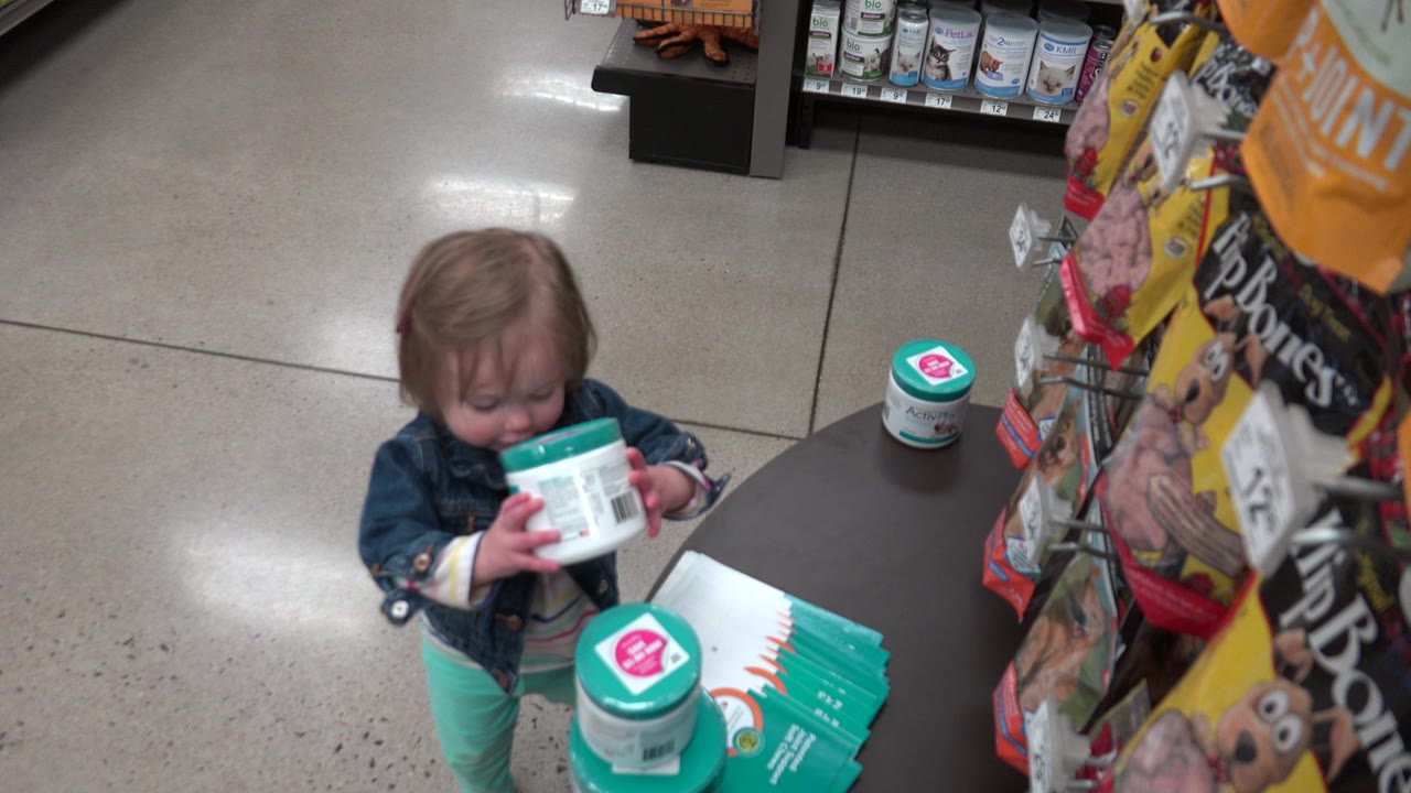 Young girl holding a white container beside a store display.