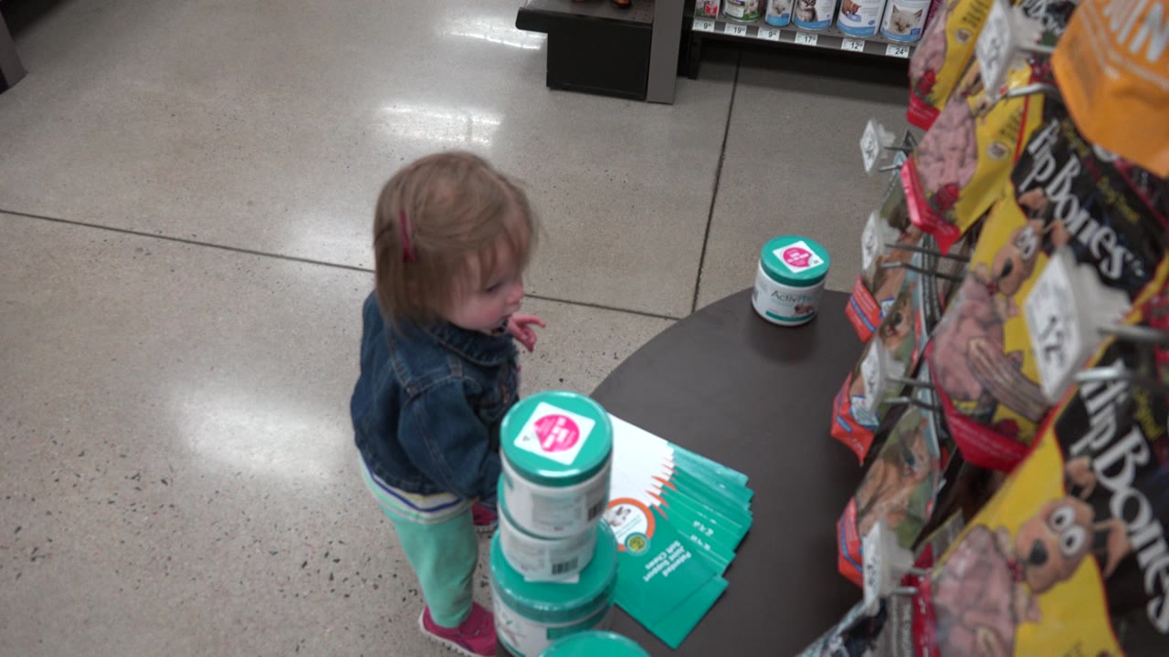 The child looks down toward the display table while standing close to teal packaged products in the Denver store aisle.