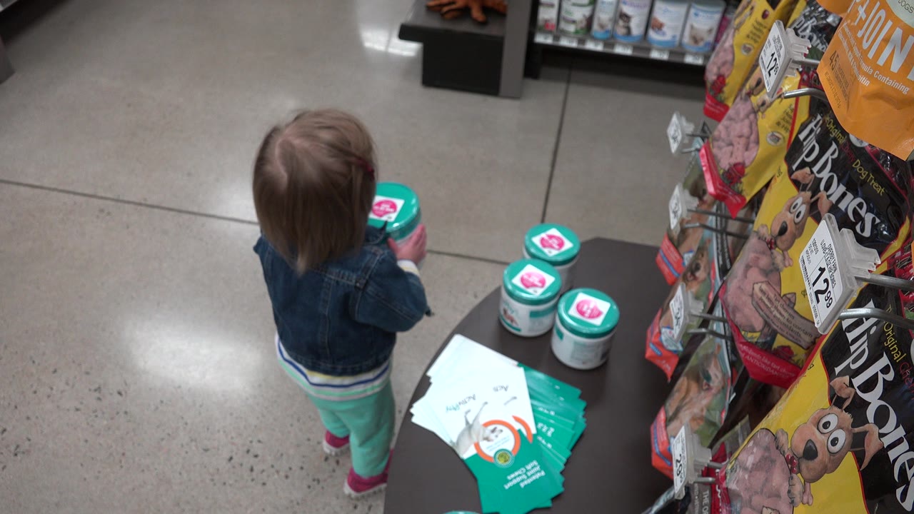 In Denver, Colorado, a small child in a denim jacket stands near teal-lidded containers and pet product packaging on a polished store floor.