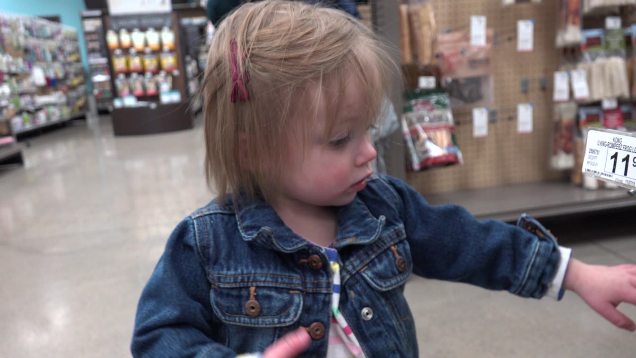 Blonde young girl in a denim jacket reaching in a supermarket aisle.
