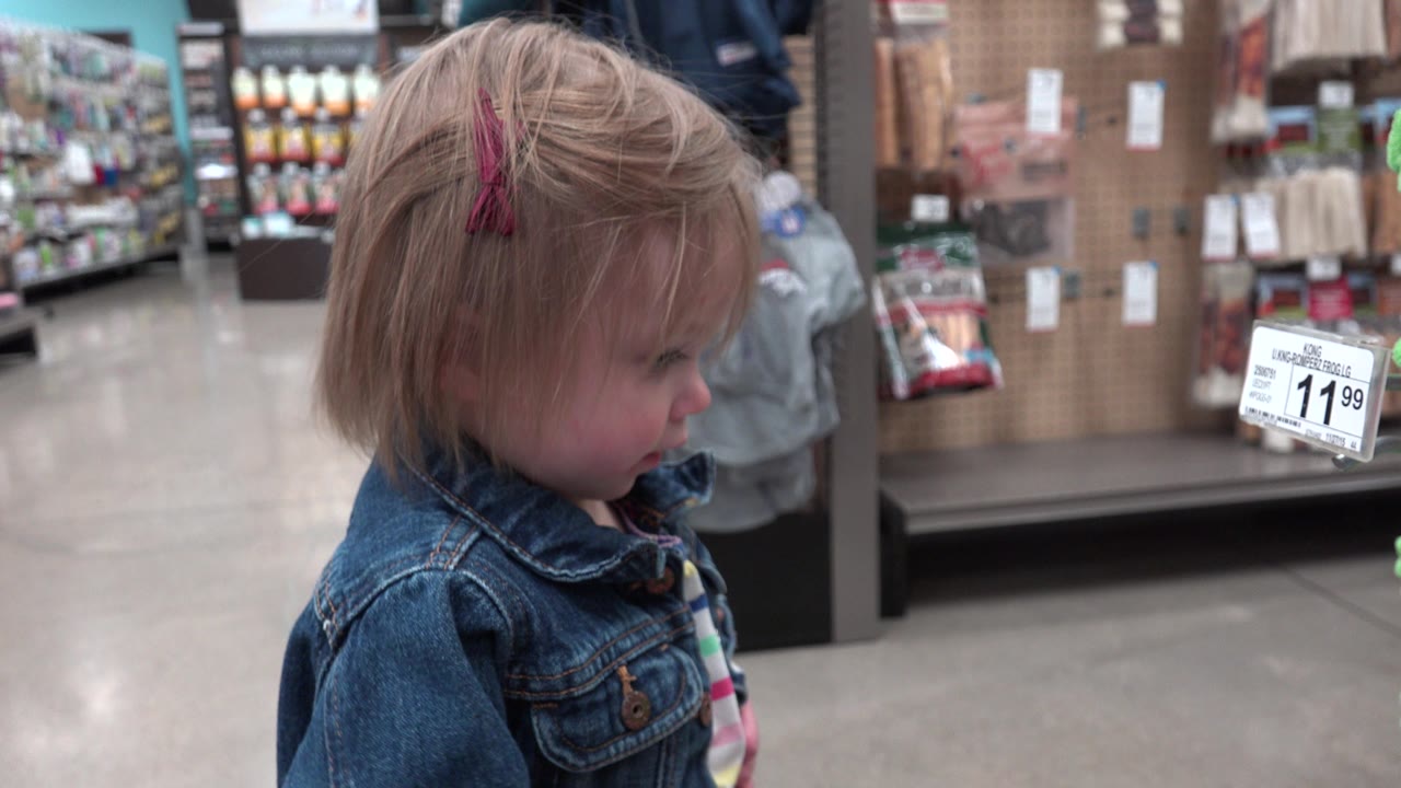 The child remains in side profile in the Denver store aisle, with a white price tag and display shelves visible to the right.