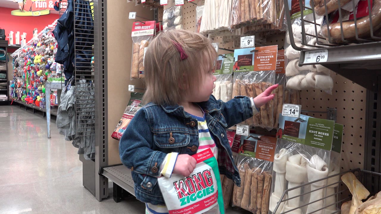 Young girl holding a package beside a store shelf of dog chews.