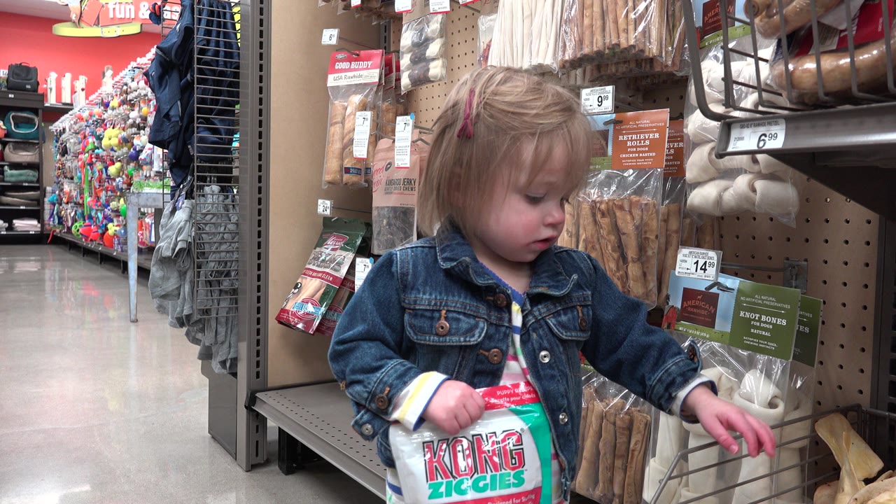 The girl looks down at items near her hands while standing beside hanging pet treats and rawhide-style bones in the Denver store aisle.