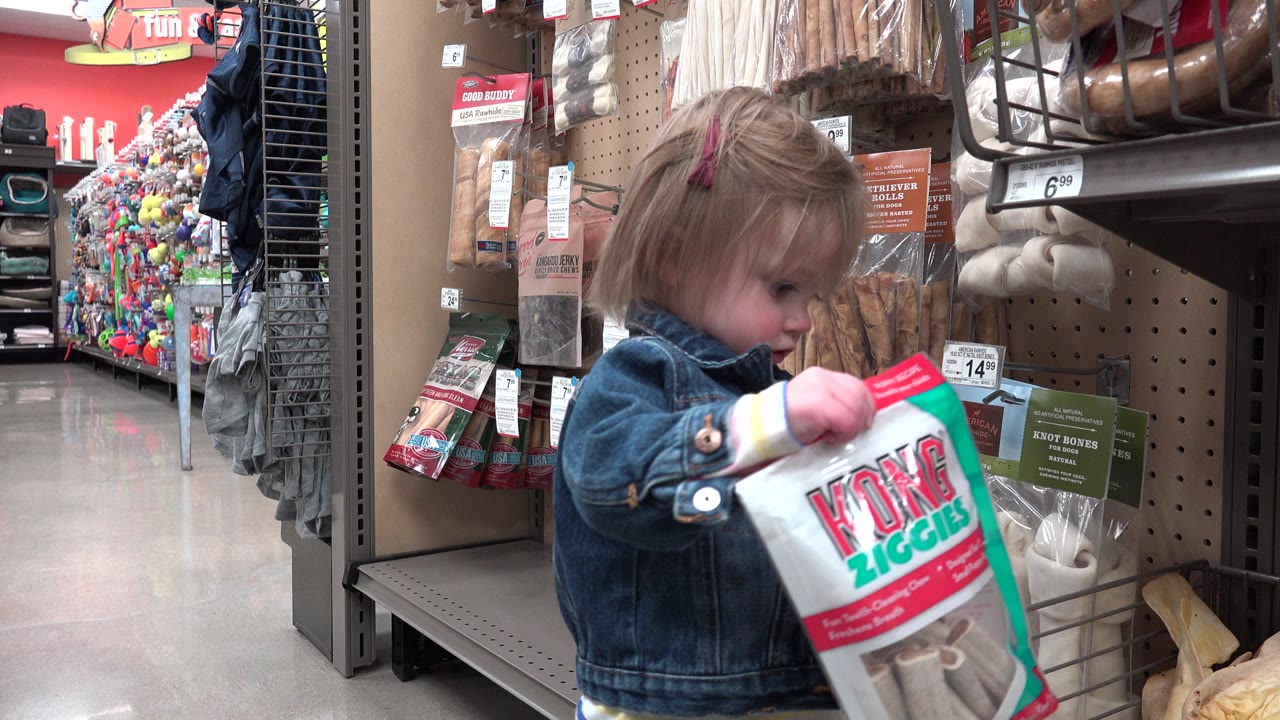 Young girl holding a dog treat bag in a pet store aisle.