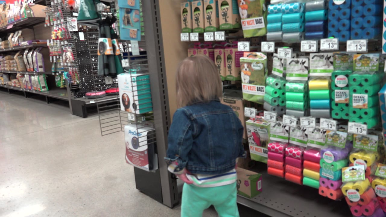 The child remains near the right-side shelves of pet products, with an empty polished aisle stretching ahead inside the Denver retail store.