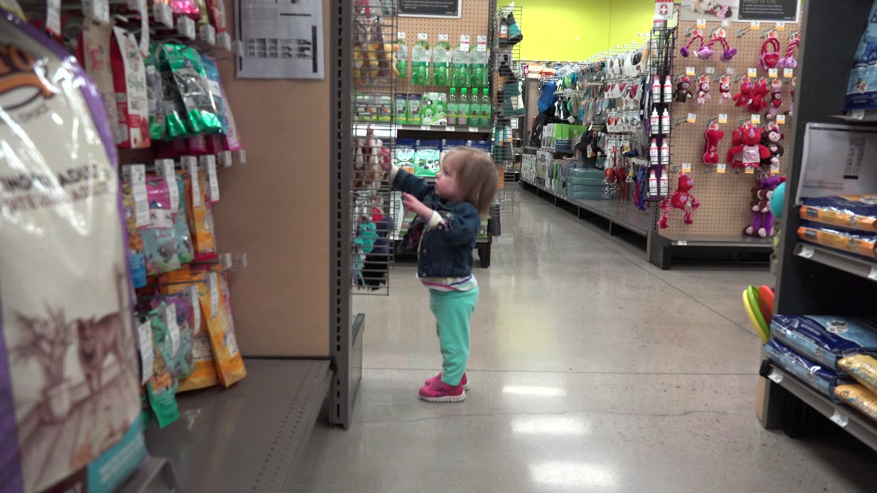 Young girl reaches toward hanging products in a store aisle.