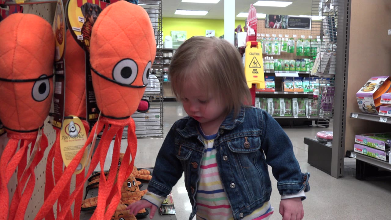 Child beside orange plush octopus toys in a store aisle.