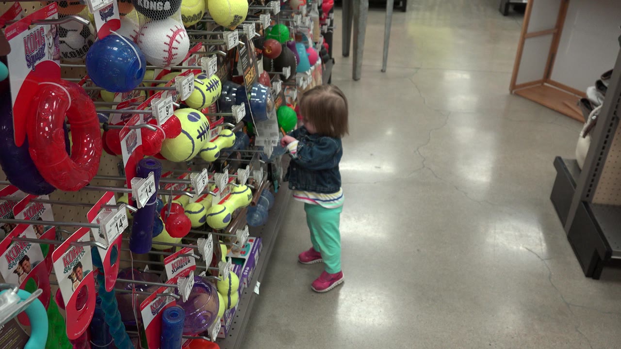 Young child standing beside a colorful toy shelf in a store aisle.
