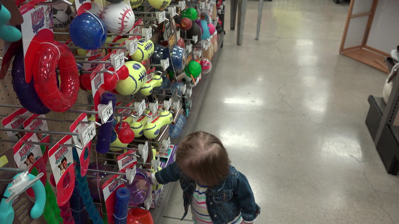 Child beside a colorful sporting goods toy display in a store aisle.