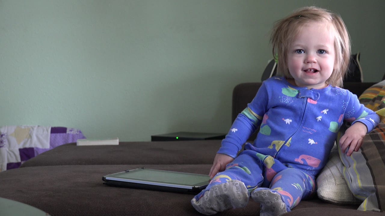 Toddler in blue pajamas sitting on a couch and smiling.