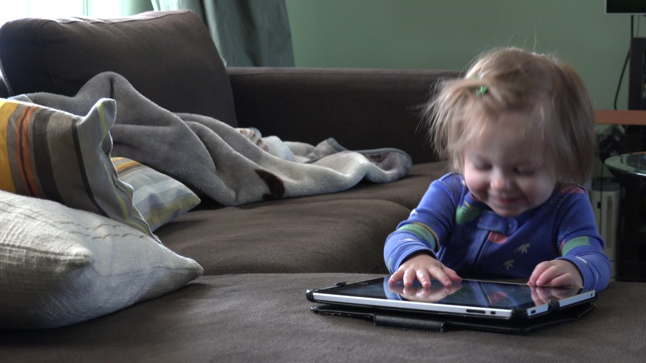 In Westminster, Colorado, the girl looks down toward the laptop as her hands touch the device, with the couch and pillows remaining static behind her.