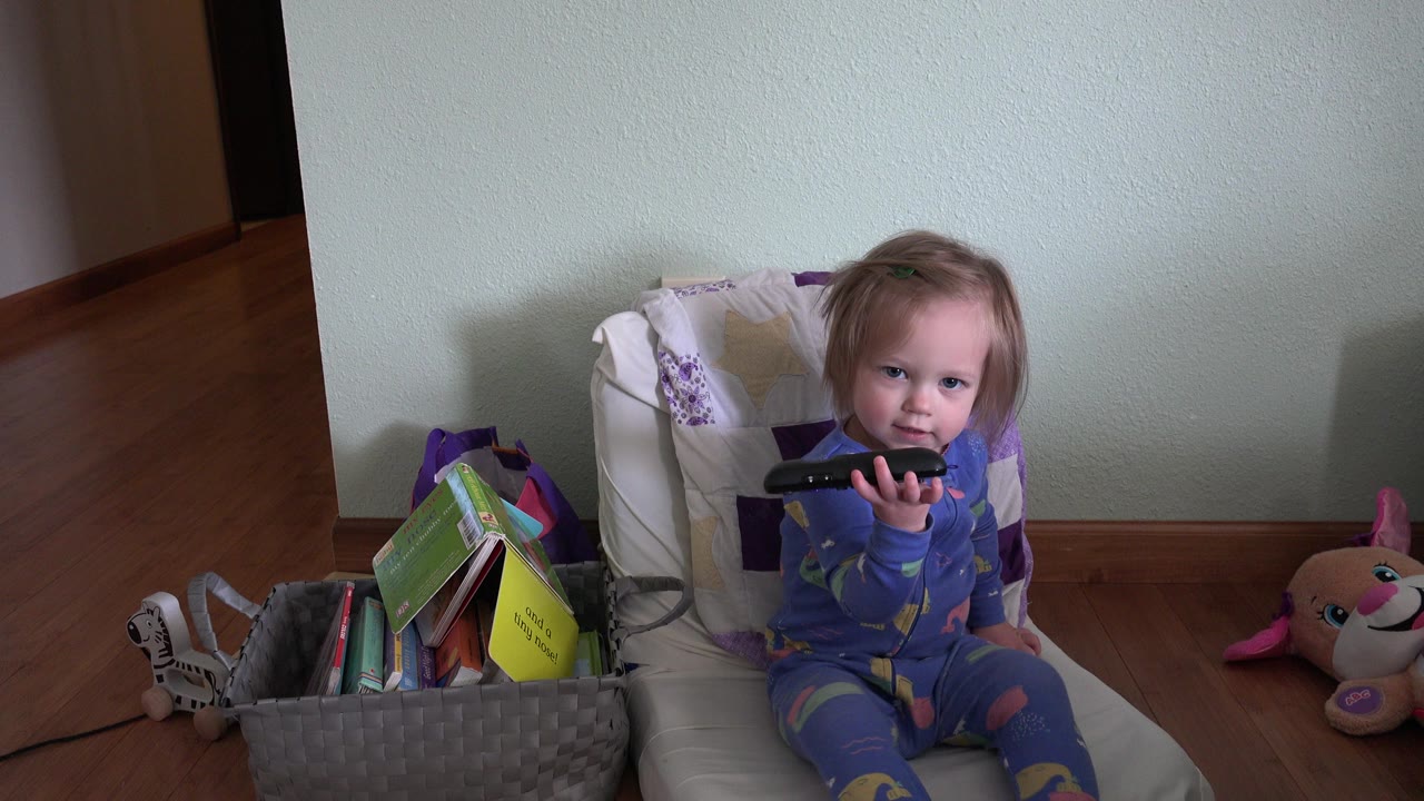 Toddler holds a remote up while sitting on a cushion.